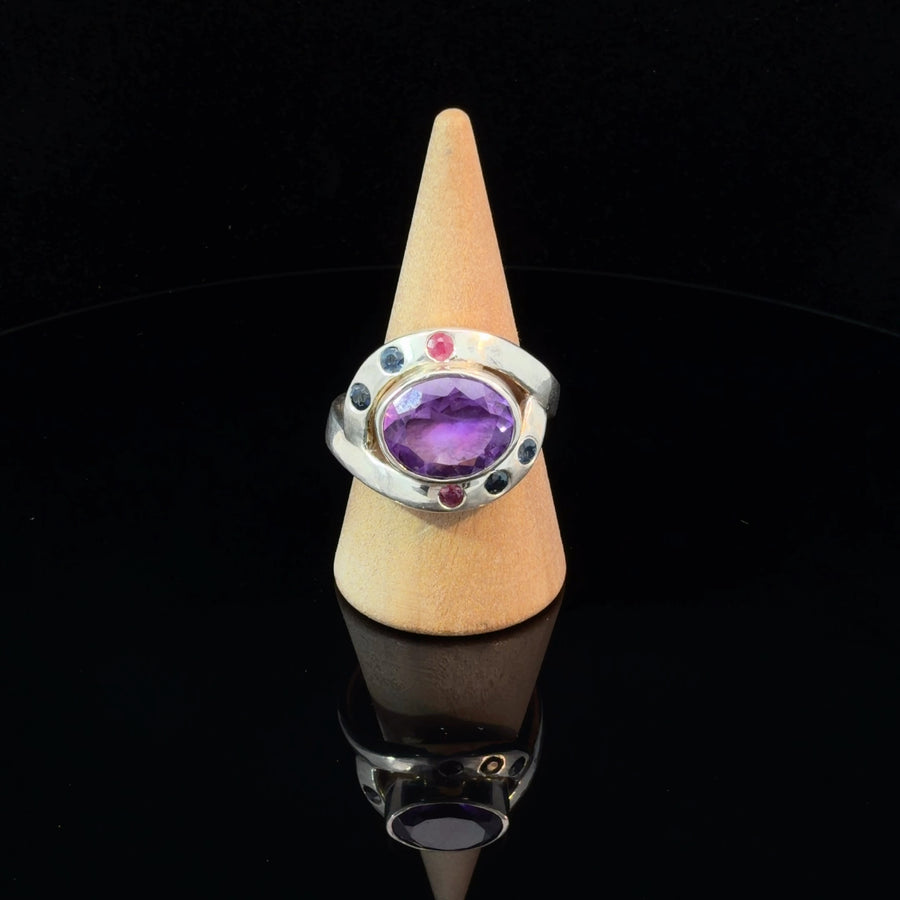 Handcrafted sterling silver statement ring featuring a large natural dark amethyst with two rubies and four flush-set blue sapphires on a thick artisan band, size 11.