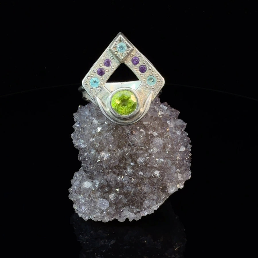 Handcrafted sterling silver size 10 ring featuring a natural Peridot center stone with three light blue Apatite gemstones and four Amethyst accents in a celestial-inspired artisan design.