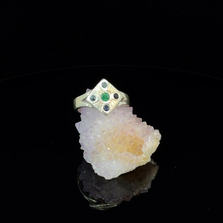 Handcrafted sterling silver ring featuring a natural emerald center stone surrounded by blue sapphire gemstones with detailed hand engraved artisan design, size 7.5.
