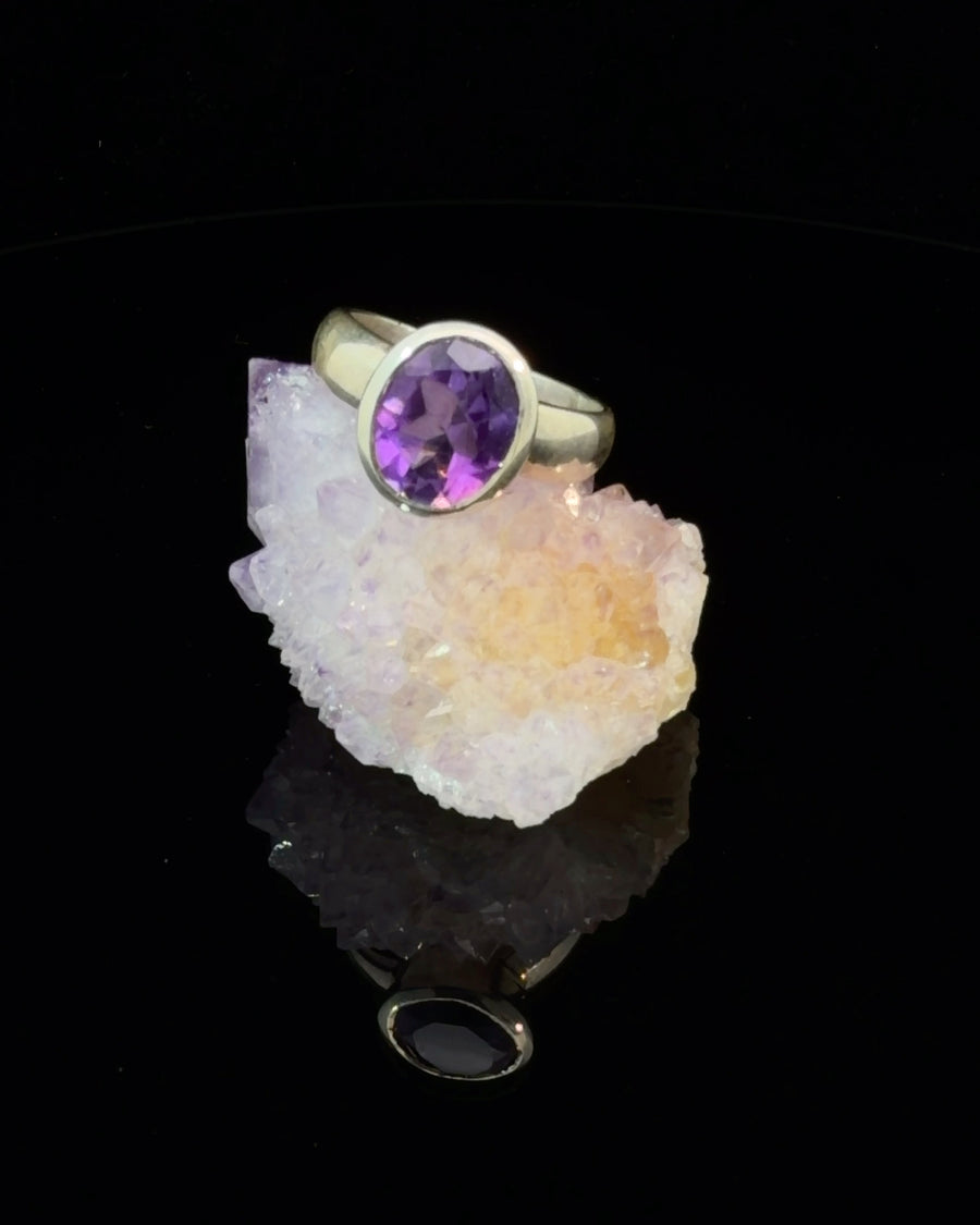 Natural oval-cut amethyst bezel set silver solitaire ring with a polished wide band, modern minimalist purple gemstone jewelry, size 6.
