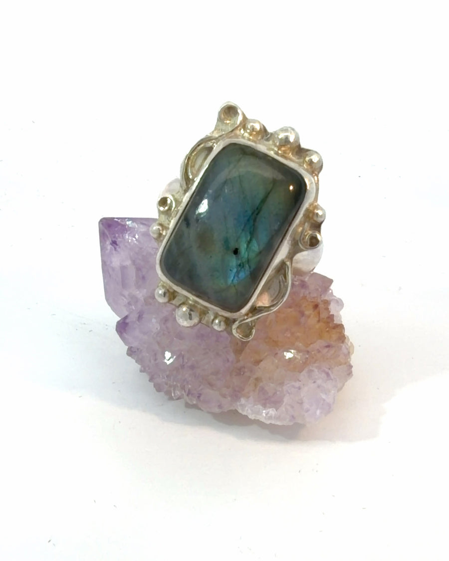 Handcrafted sterling silver Size 8 cocktail ring featuring a natural rectangular Labradorite cabochon in a bezel setting with decorative silver beadwork and swirling bohemian accents.
