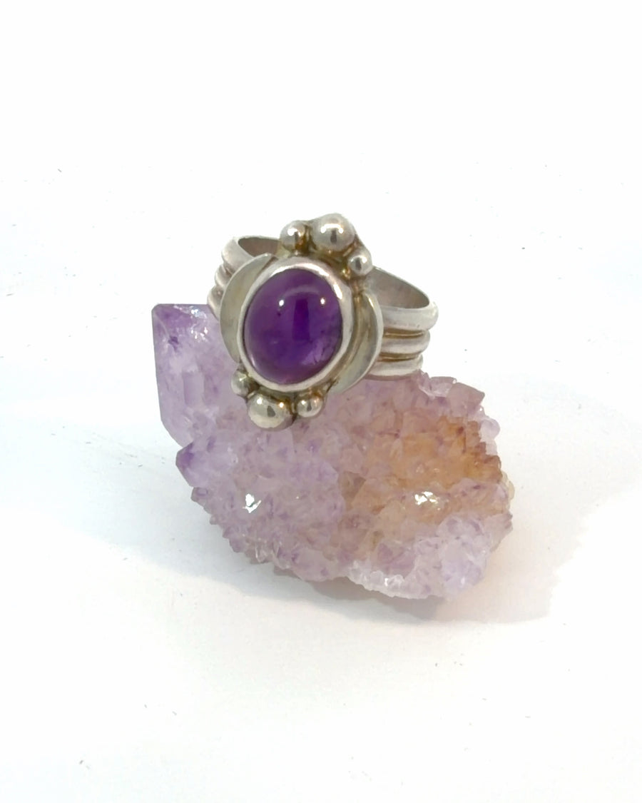 Handcrafted sterling silver Size 7 cocktail ring featuring a natural oval Amethyst cabochon in a bezel setting with decorative silver bead accents and a triple band.