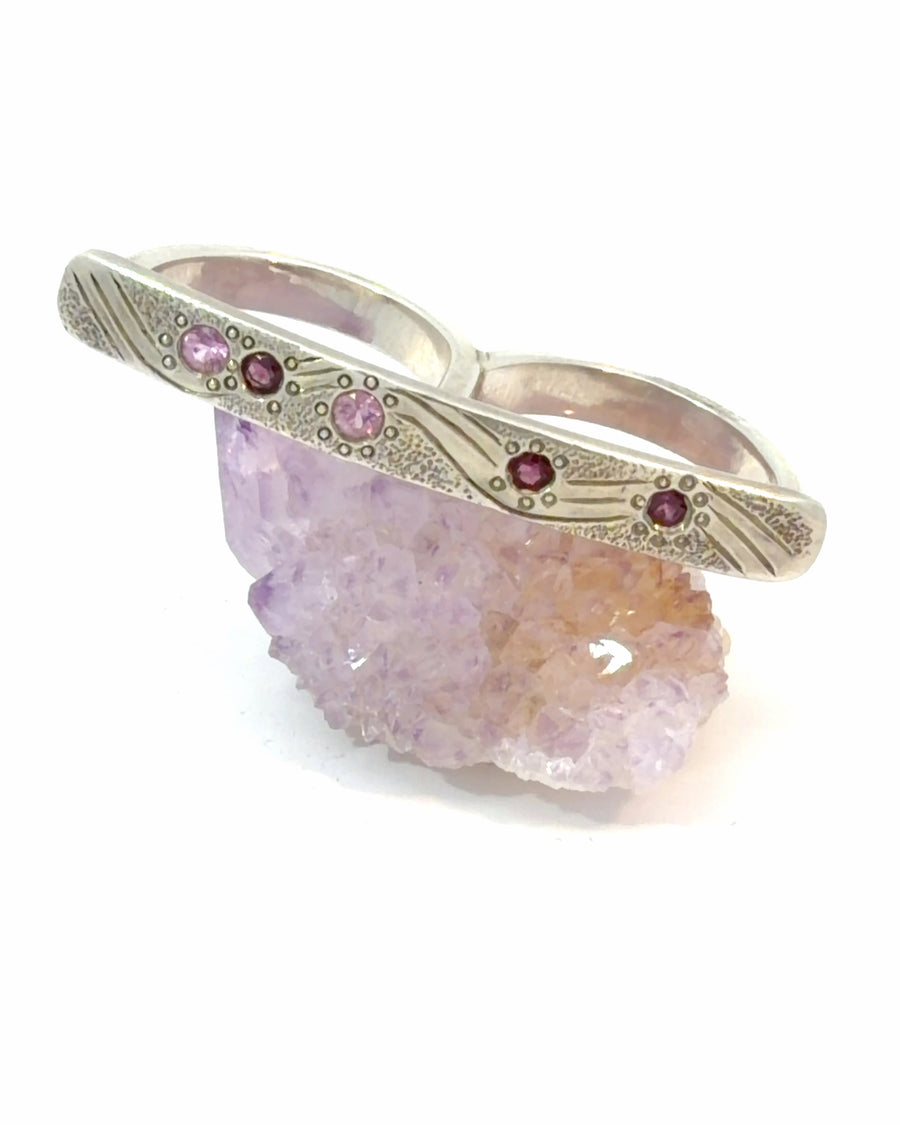 Handcrafted sterling silver two-finger ring with engraved wave design and faceted Pink Sapphire gemstones in sizes 7 and 6.5.
