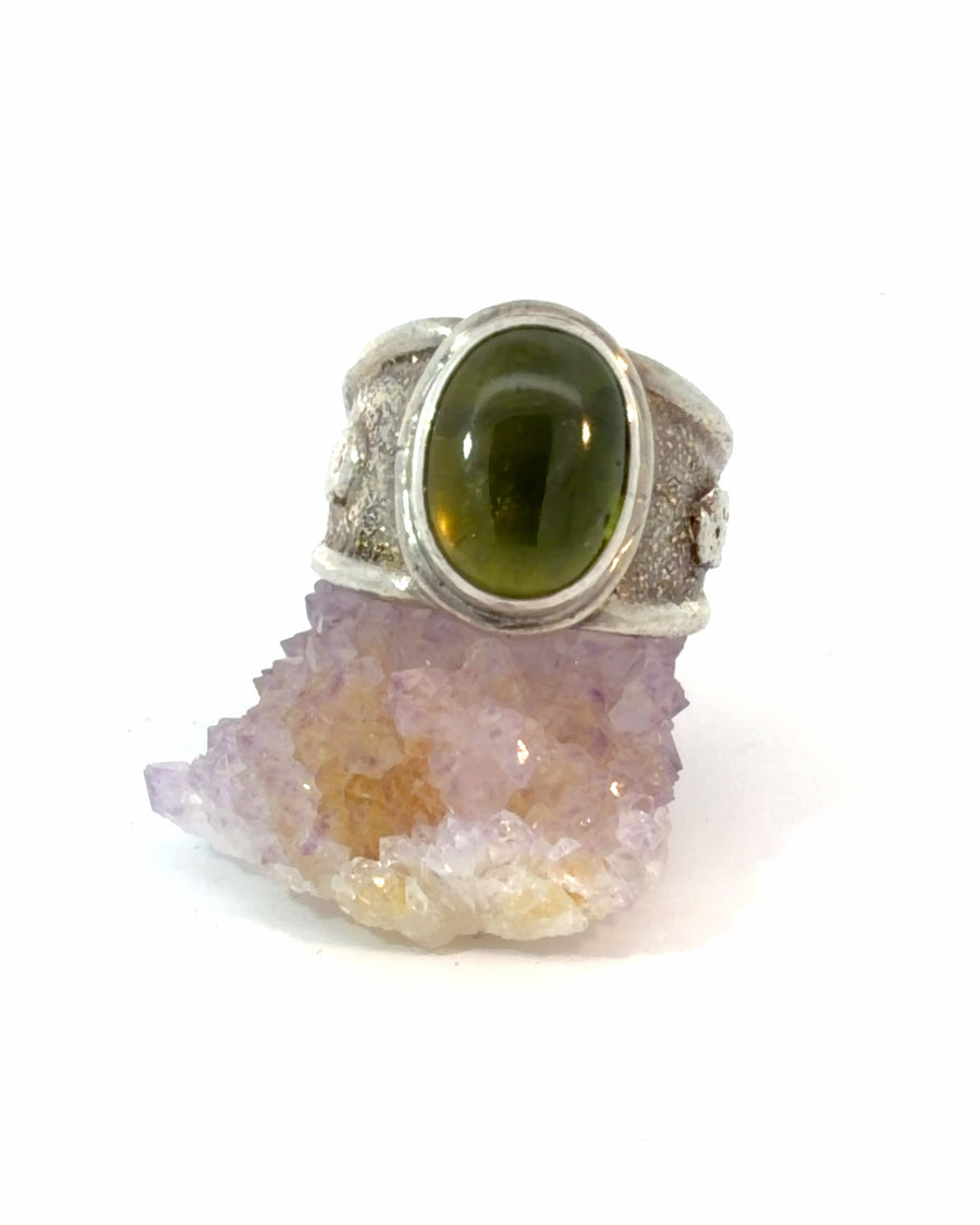Handcrafted adjustable sterling silver ring featuring a natural oval green Vesuvianite cabochon in a bezel setting with a heavily textured wide silver band.

