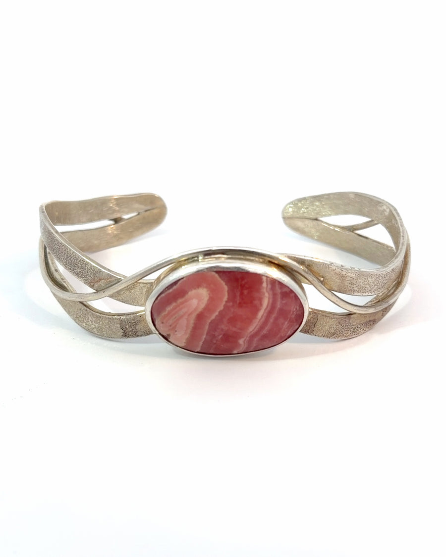 Handcrafted sterling silver cuff bracelet featuring a natural oval Rhodochrosite gemstone with white banding in a bezel setting and textured artisan silver bands.