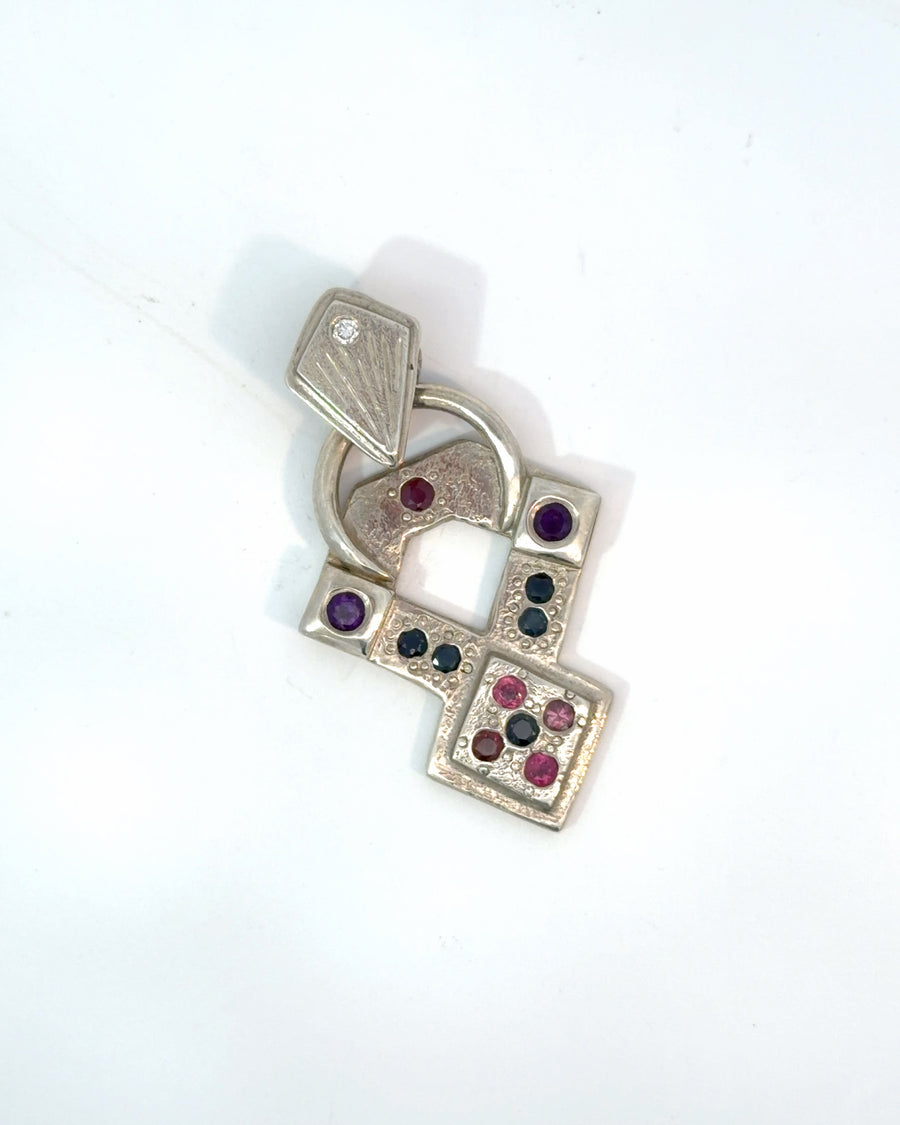 Handcrafted sterling silver geometric pendant featuring bezel-set red rubies, dark accent gemstones, textured silver surfaces, and a modern artisan design.