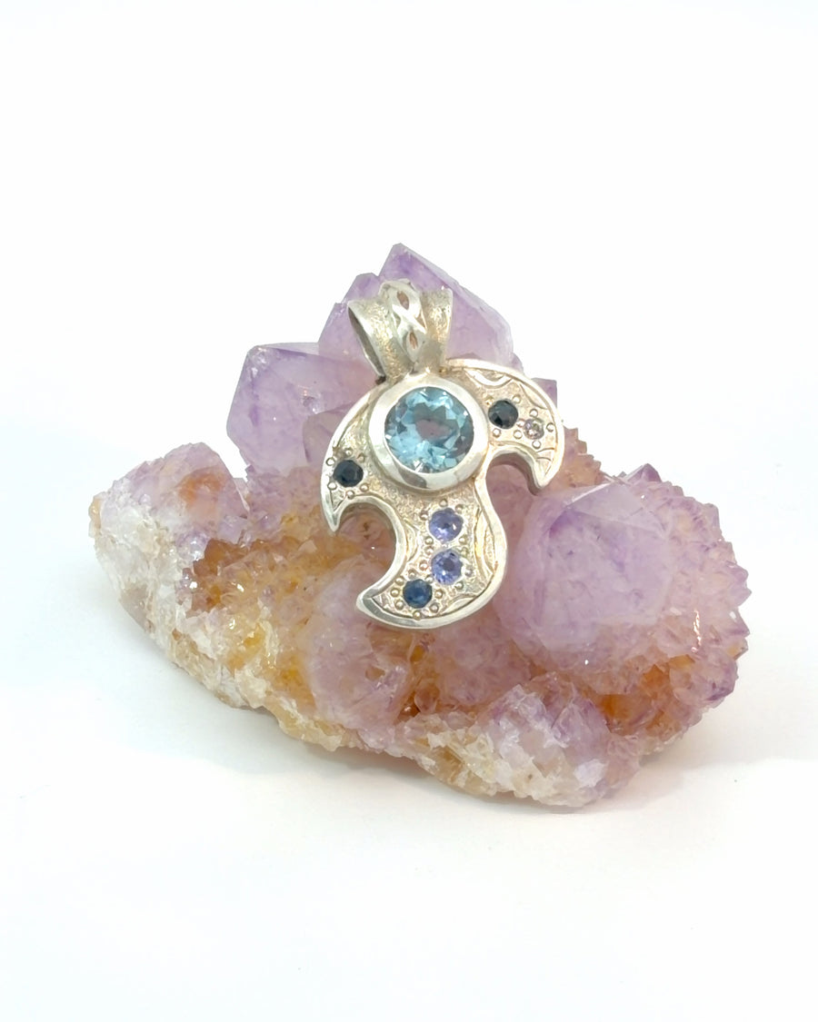 Handcrafted sterling silver pendant featuring a blue topaz centerpiece with textured metalwork and smaller blue gemstone accents.