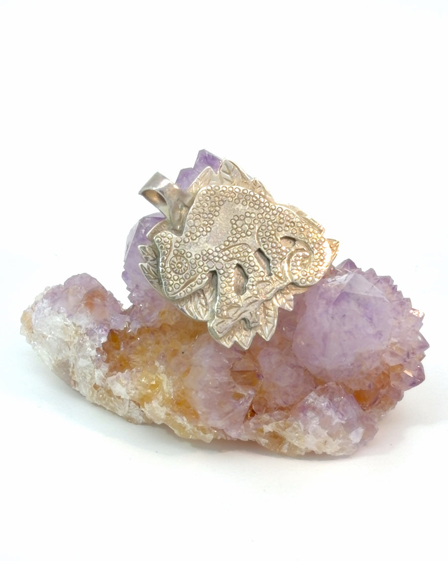 Handcrafted silver chameleon pendant with detailed scales, curled tail, and carved leaf background.