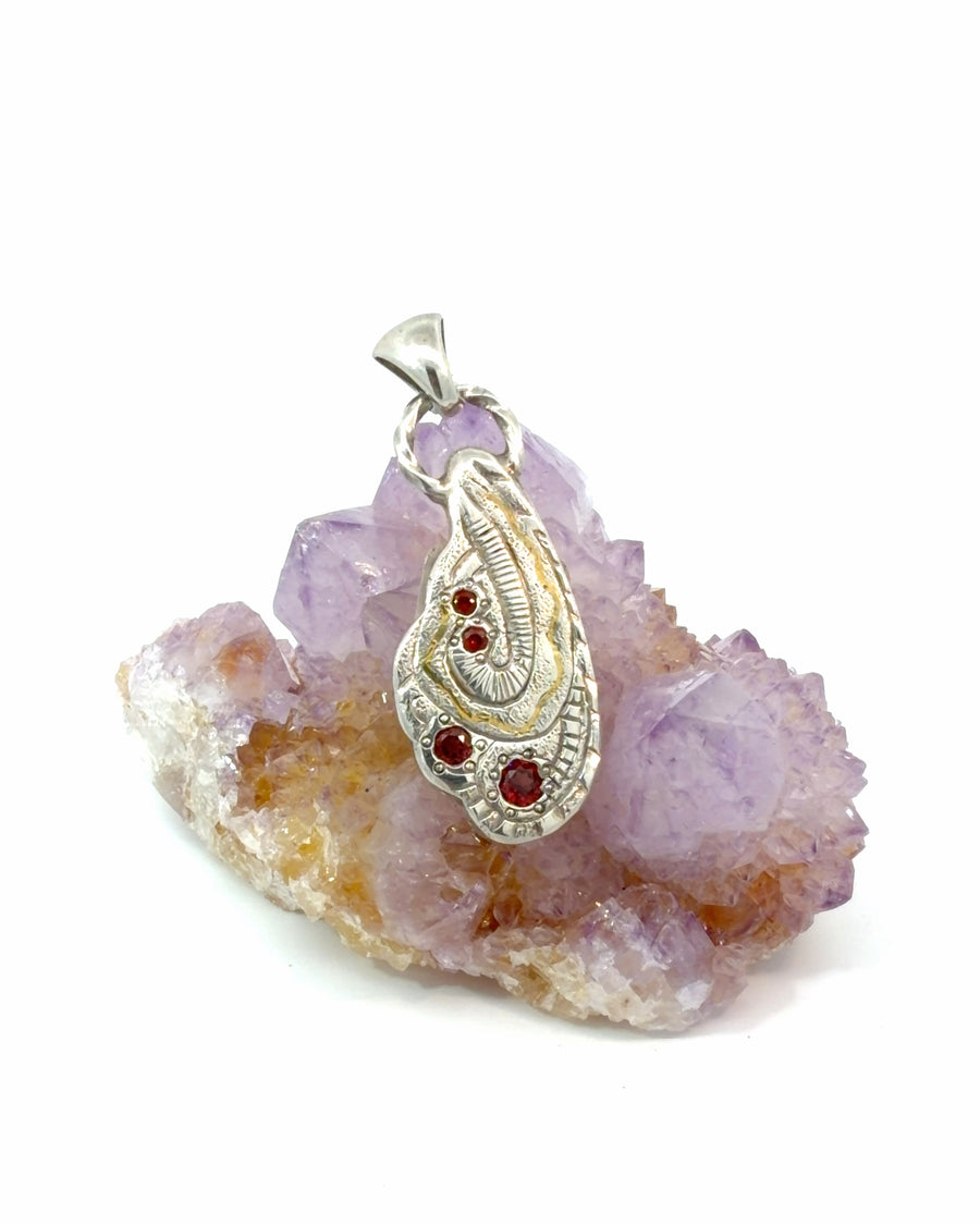 Handcrafted silver pendant featuring four round garnets, flowing 24K gold inlay, and intricate organic sculptural textures.