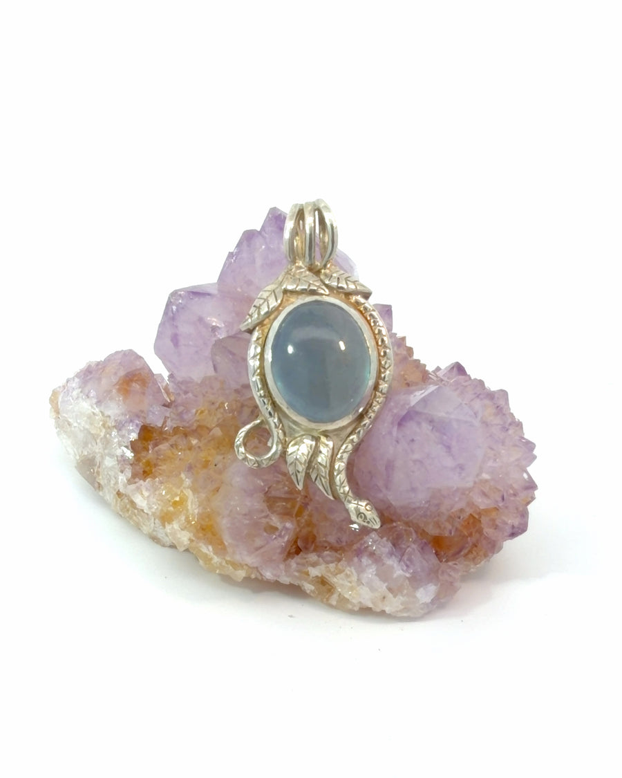 Handcrafted sterling silver aquamarine pendant featuring a cabochon aquamarine gemstone surrounded by an intricately detailed snake with textured scales and leaf accents.