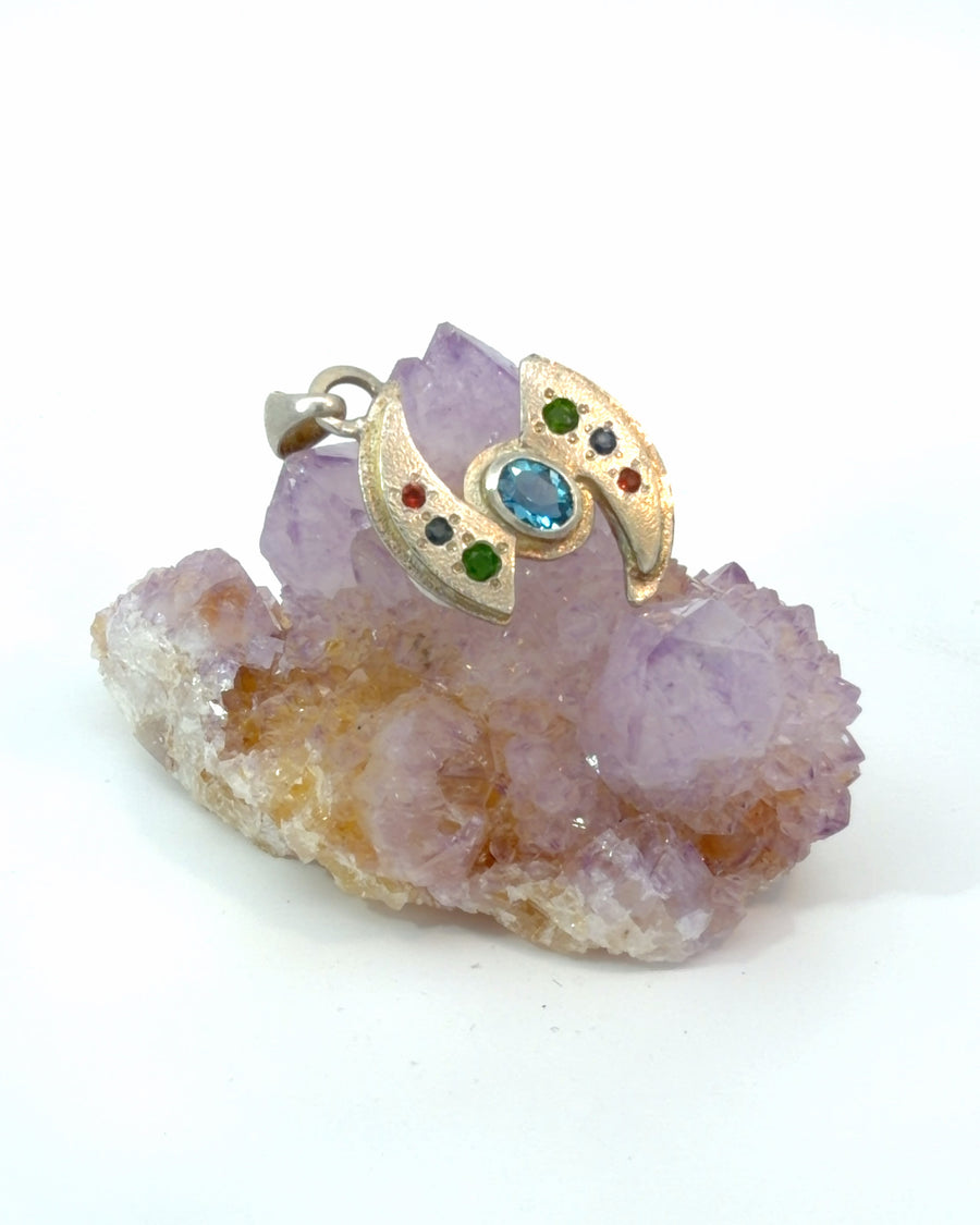 Handcrafted sterling silver pendant featuring an oval blue topaz in a bezel setting with textured wing details and multicolor gemstone accents.