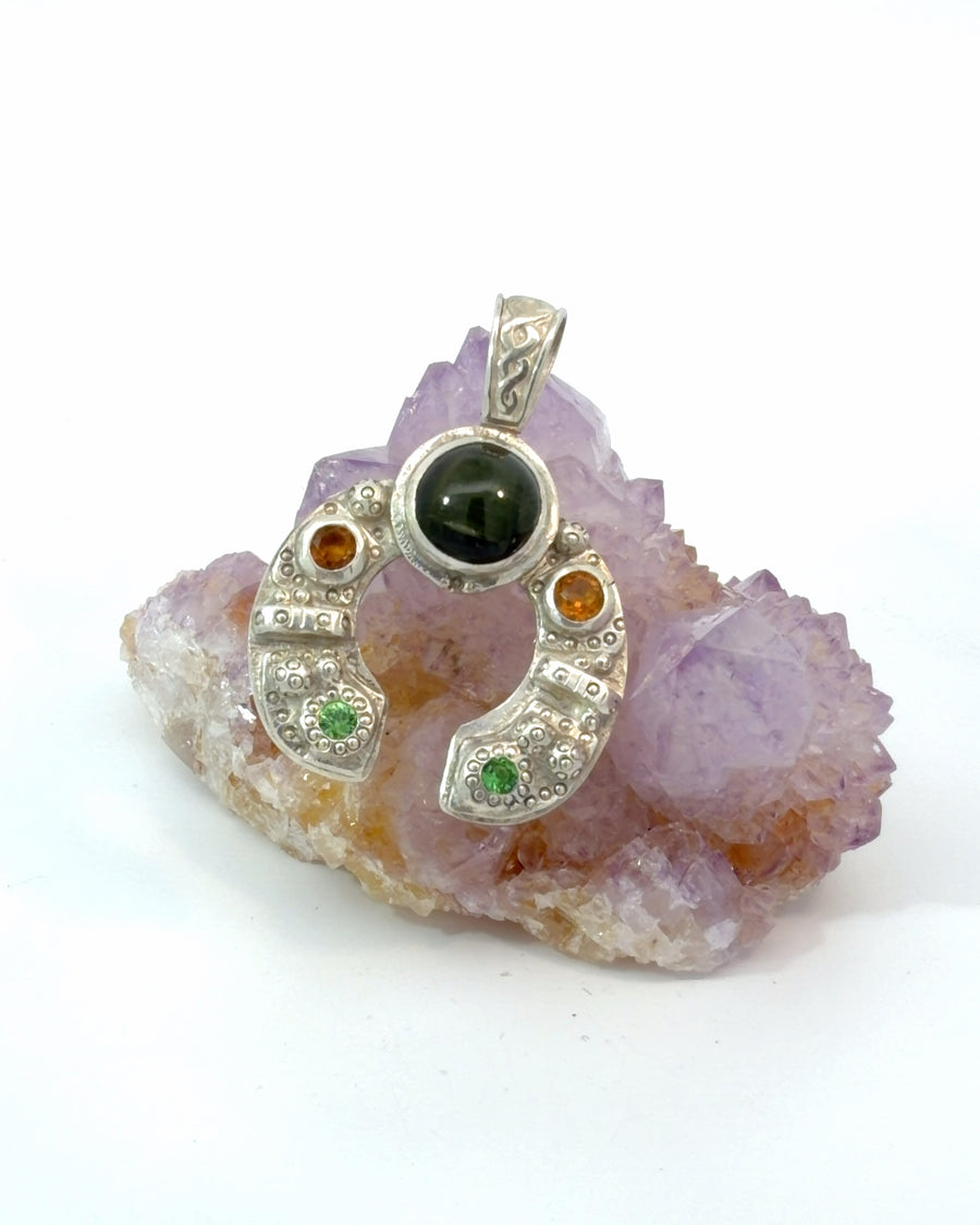 Handcrafted sterling silver pendant featuring a natural black tourmaline cabochon with orange and green gemstone accents in a textured horseshoe-inspired design.
