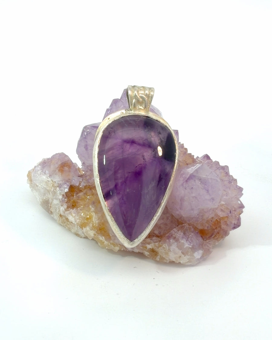 Handcrafted sterling silver pendant featuring a natural pear-shaped amethyst cabochon with rich purple color banding in a polished bezel setting.
