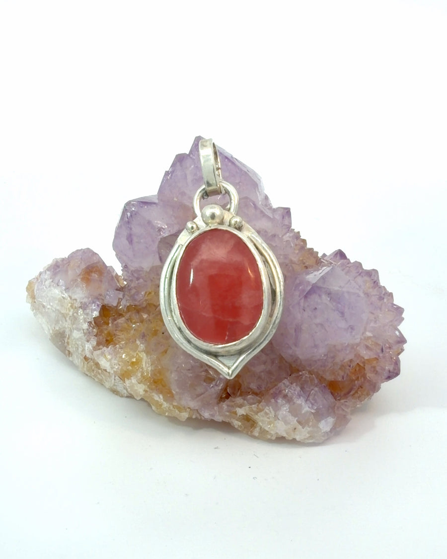 Handcrafted oval Rhodochrosite pendant in sterling silver with a polished bezel setting and artisan bead accents.