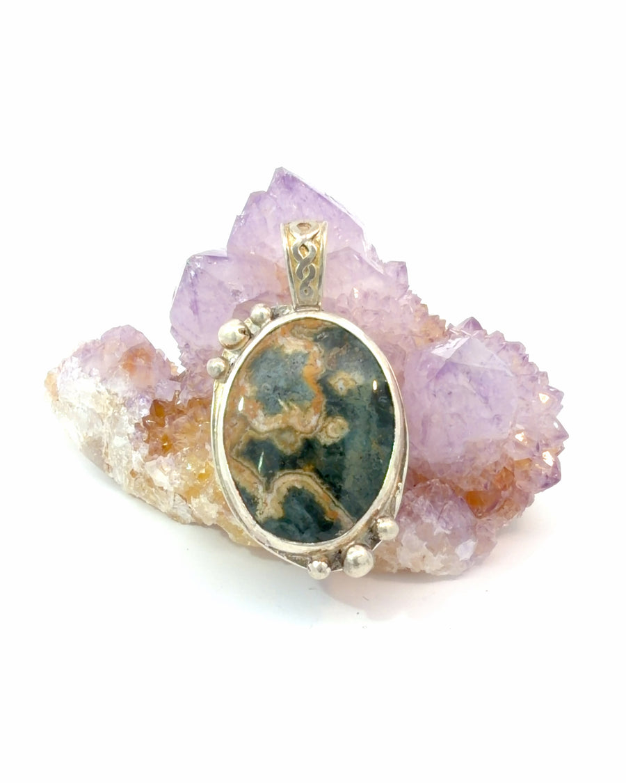Handcrafted sterling silver pendant featuring a large oval Ocean Jasper gemstone with green, brown, and white patterns in a bezel setting with silver bead accents.