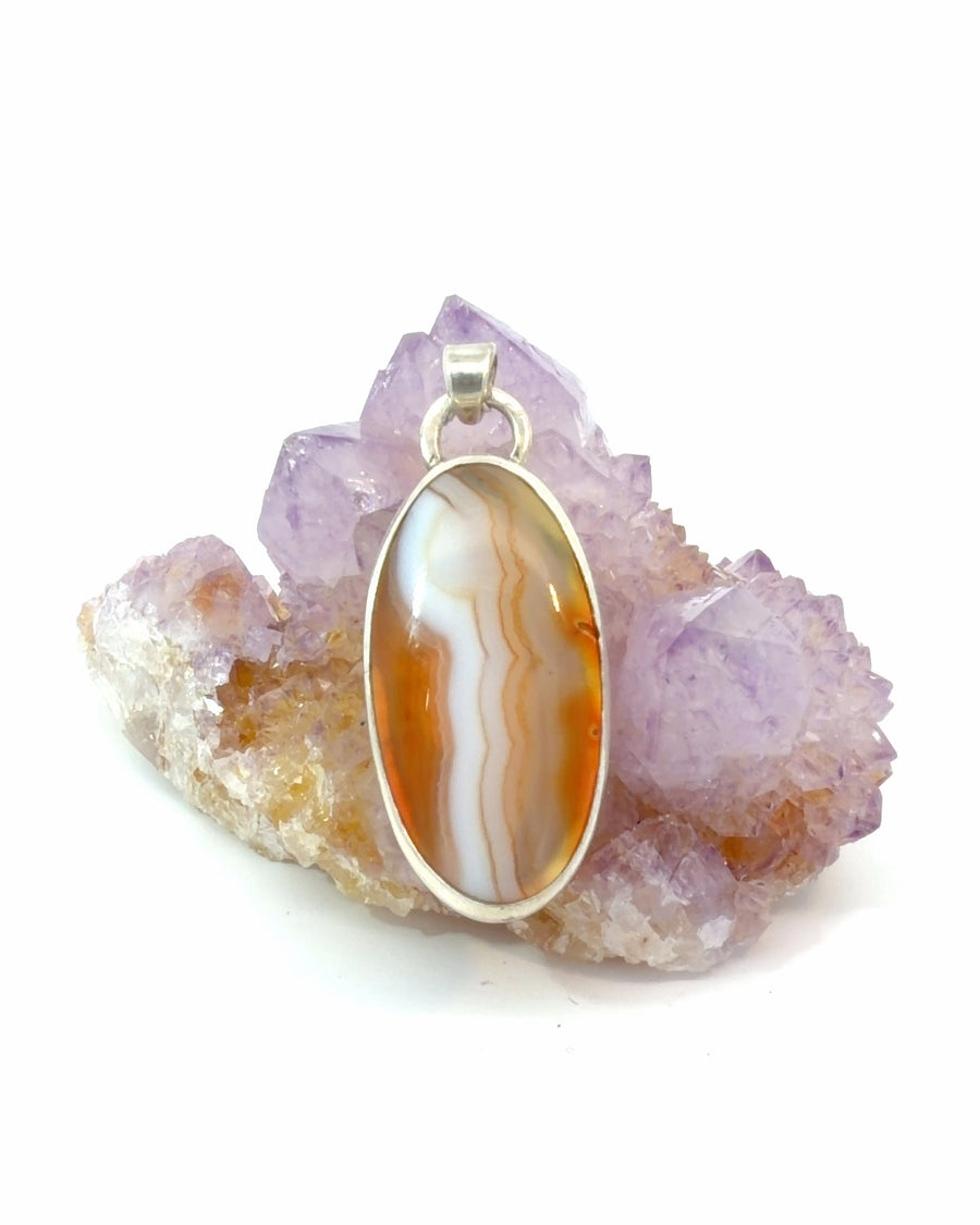 Natural orange banded agate oval cabochon pendant in sterling silver bezel setting with warm orange and white gemstone patterns.