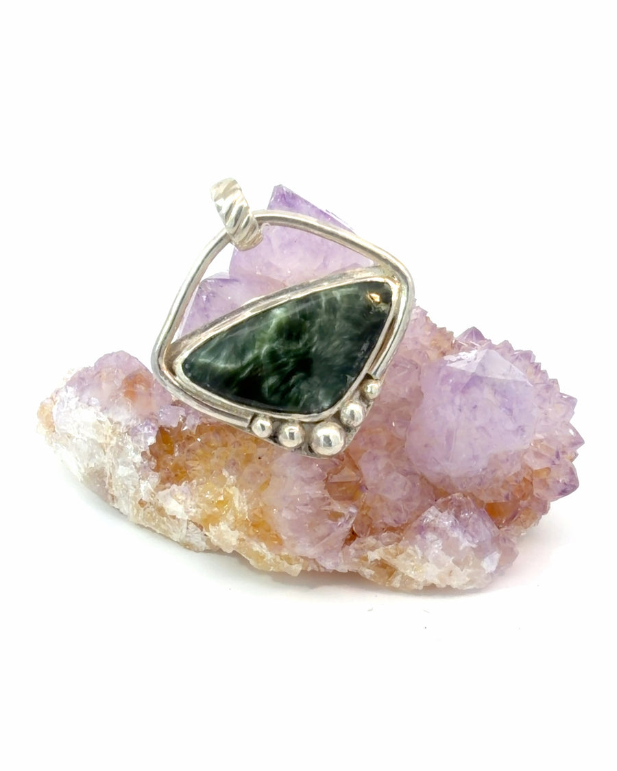 Handcrafted sterling silver pendant featuring a natural Seraphinite cabochon with feather-like patterns, asymmetrical open-frame design, and polished silver bead accents.