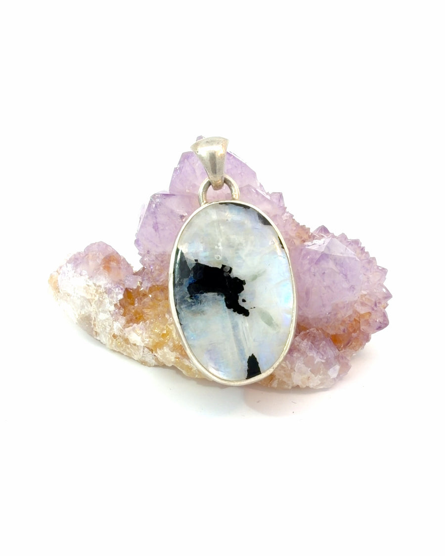 Unique moonstone pendant featuring bold black inclusions, a sterling silver bezel setting, and natural adularescence. One-of-a-kind gemstone jewelry.
