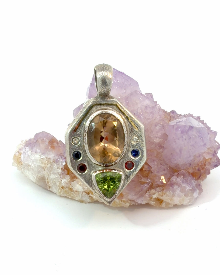 Handcrafted oxidized sterling silver pendant featuring a large bezel-set oval citrine, trillion-cut green gemstone, and blue, red, and clear accent stones with intricate geometric textured detailing.
