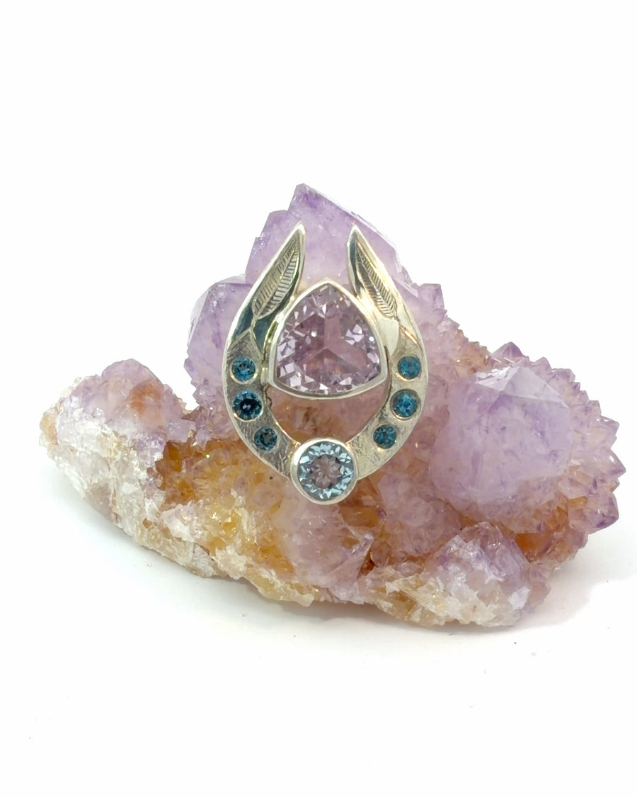 Sterling silver horseshoe pendant featuring a trillion-cut Kunzite gemstone with blue Topaz accents and engraved leaf details.