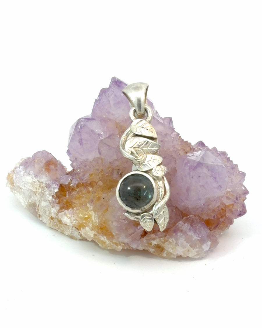 Sterling silver pendant featuring intricate leaf and vine details surrounding a bezel-set round tourmaline gemstone.