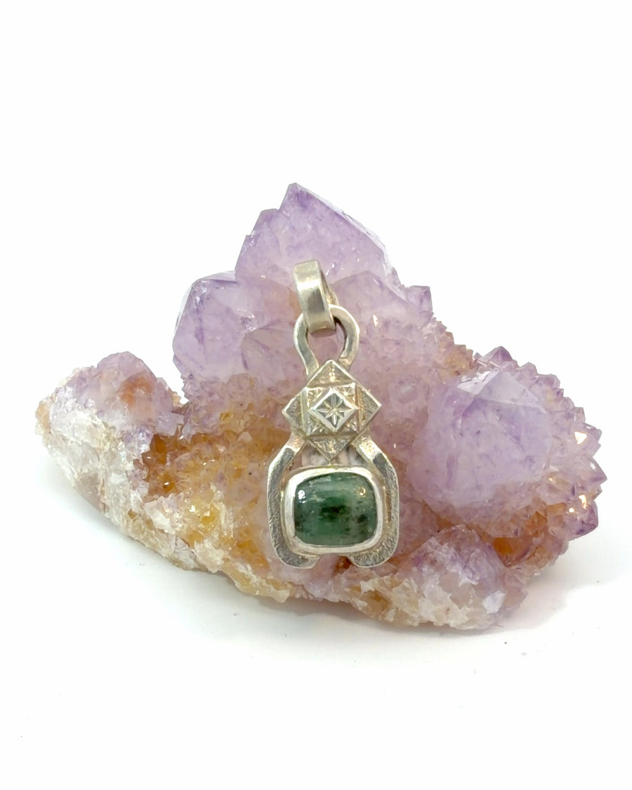 Handcrafted sterling silver pendant featuring a bezel-set green emerald cabochon beneath a geometric diamond-shaped motif with engraved star detail and textured artisan finish.