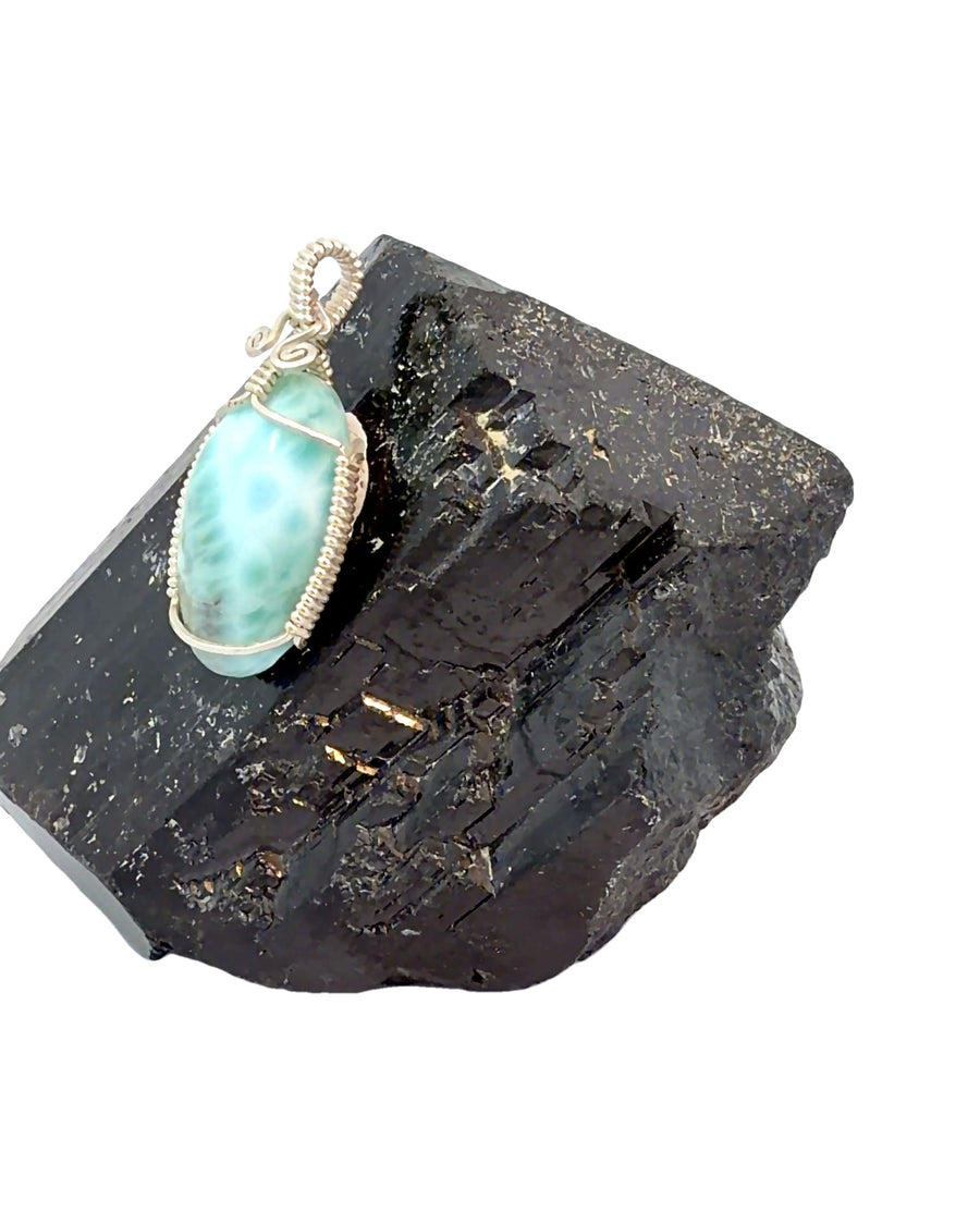 a handcrafted sterling silver wire wrapped pendant featuring a natural Larimar cabochon with tranquil ocean-blue hues.